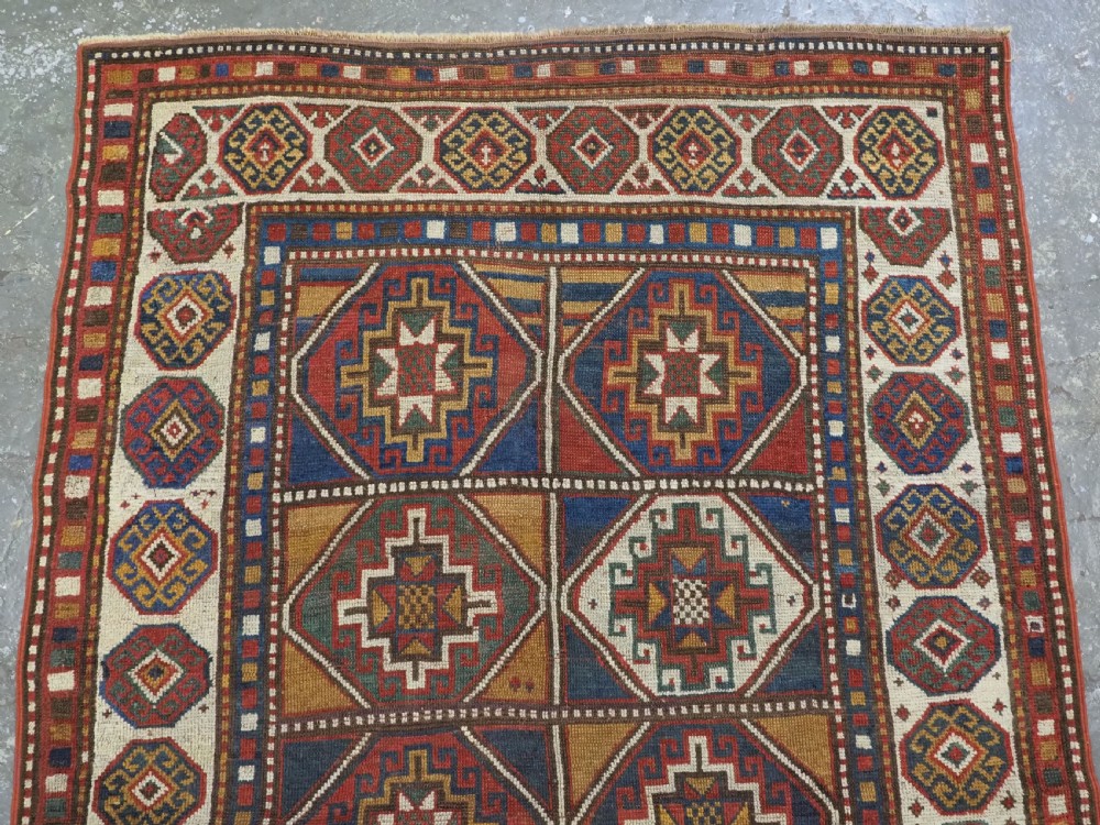 An antique hand-knotted Caucasian Moghan Kazak wool rug featuring a grid of geometric latch-hook medallions framed by patterned borders. View III