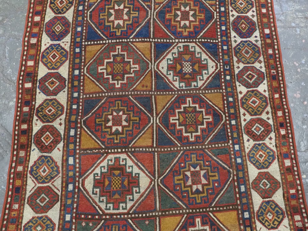 An antique hand-knotted Caucasian Moghan Kazak wool rug featuring a grid of geometric latch-hook medallions framed by patterned borders. View IV