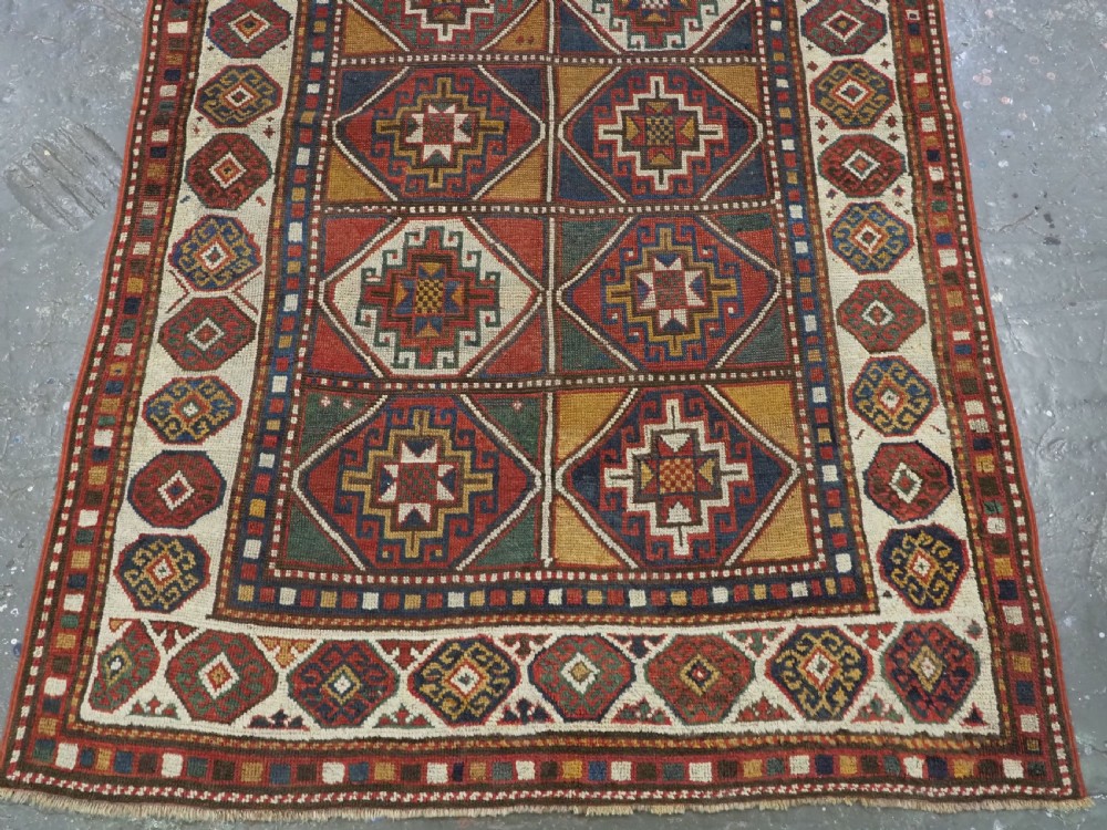 An antique hand-knotted Caucasian Moghan Kazak wool rug featuring a grid of geometric latch-hook medallions framed by patterned borders. View V