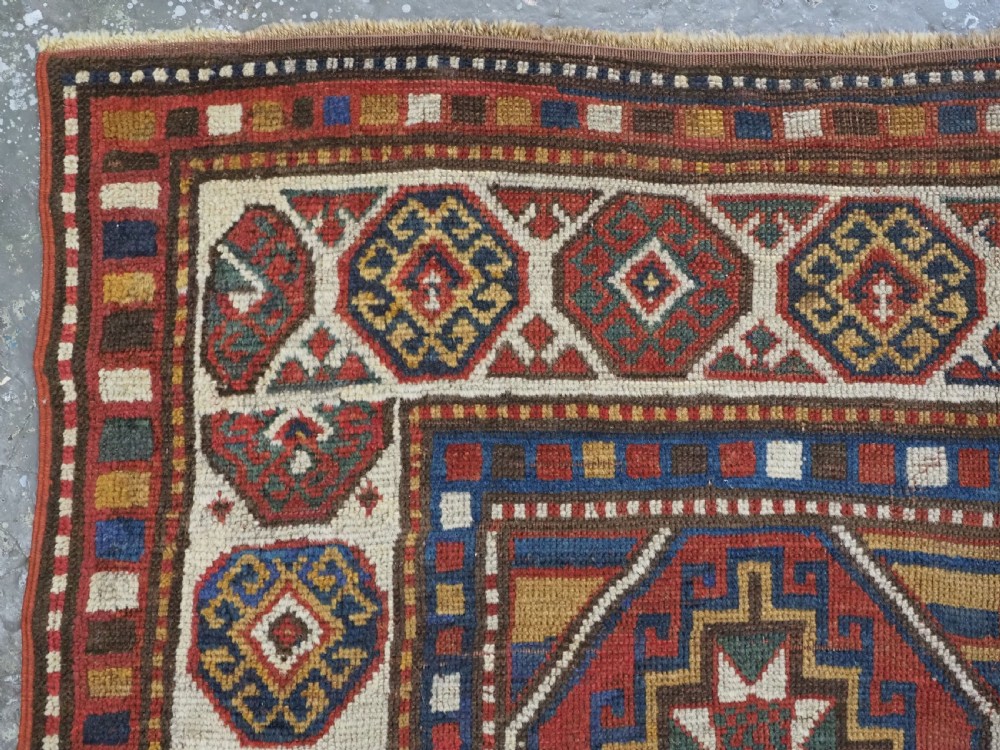An antique hand-knotted Caucasian Moghan Kazak wool rug featuring a grid of geometric latch-hook medallions framed by patterned borders. View VI
