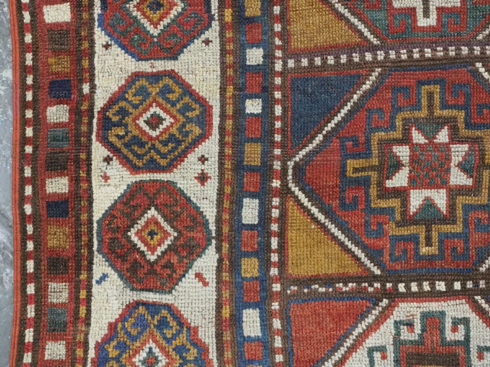 An antique hand-knotted Caucasian Moghan Kazak wool rug featuring a grid of geometric latch-hook medallions framed by patterned borders. View VII