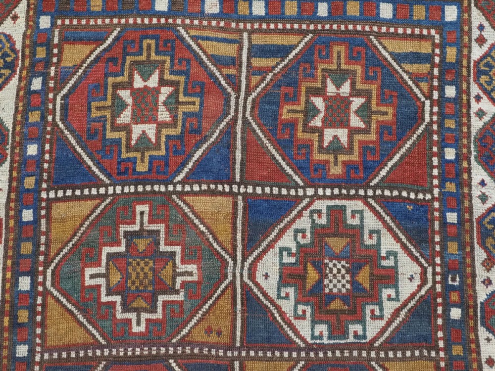 An antique hand-knotted Caucasian Moghan Kazak wool rug featuring a grid of geometric latch-hook medallions framed by patterned borders. View VIII