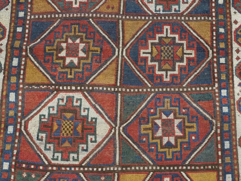 An antique hand-knotted Caucasian Moghan Kazak wool rug featuring a grid of geometric latch-hook medallions framed by patterned borders. View IX