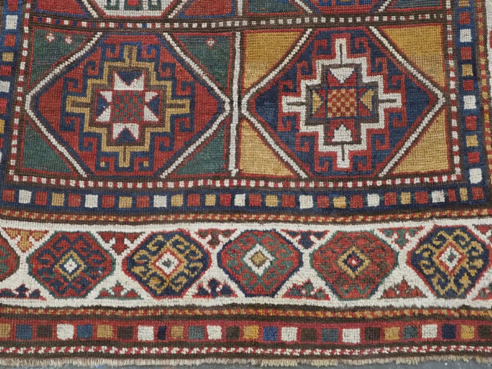 An antique hand-knotted Caucasian Moghan Kazak wool rug featuring a grid of geometric latch-hook medallions framed by patterned borders. View X