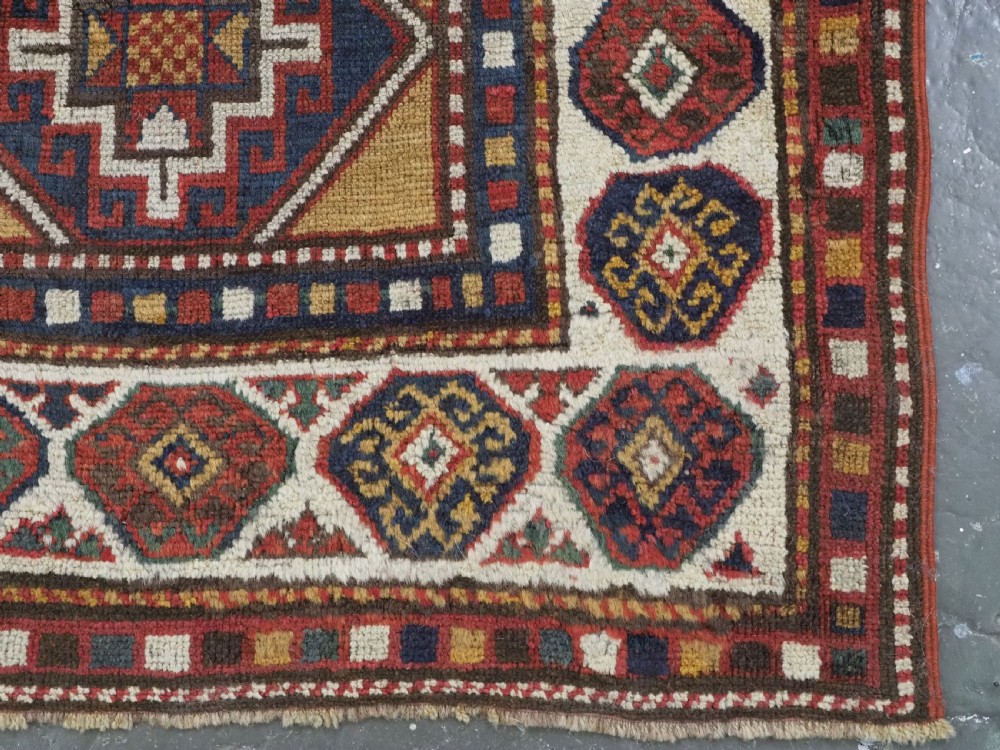 An antique hand-knotted Caucasian Moghan Kazak wool rug featuring a grid of geometric latch-hook medallions framed by patterned borders. View XI