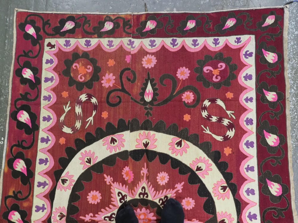 A rectangular hand-embroidered textile featuring a large central circular starburst medallion surrounded by floral motifs in shades of pink, cream, orange, and burgundy. View II