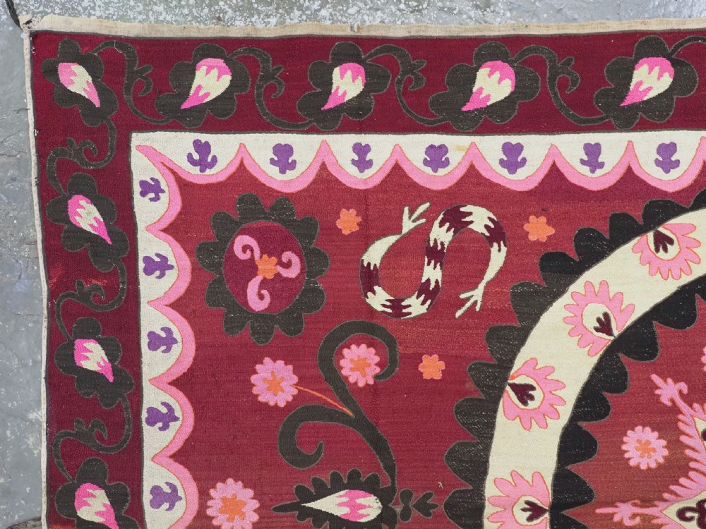 A rectangular hand-embroidered textile featuring a large central circular starburst medallion surrounded by floral motifs in shades of pink, cream, orange, and burgundy. View VI