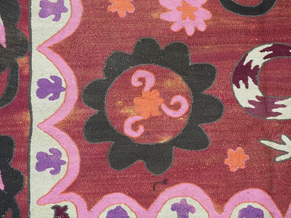A rectangular hand-embroidered textile featuring a large central circular starburst medallion surrounded by floral motifs in shades of pink, cream, orange, and burgundy. View IX