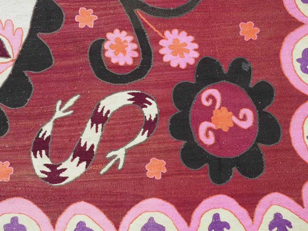 A rectangular hand-embroidered textile featuring a large central circular starburst medallion surrounded by floral motifs in shades of pink, cream, orange, and burgundy. View X