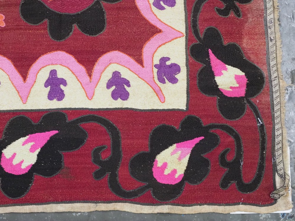 A rectangular hand-embroidered textile featuring a large central circular starburst medallion surrounded by floral motifs in shades of pink, cream, orange, and burgundy. View XI