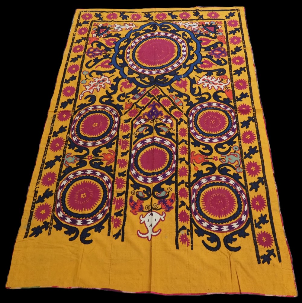 An antique Uzbek prayer suzani featuring silk embroidery with circular floral medallions and a central arch motif on a yellow cotton ground.