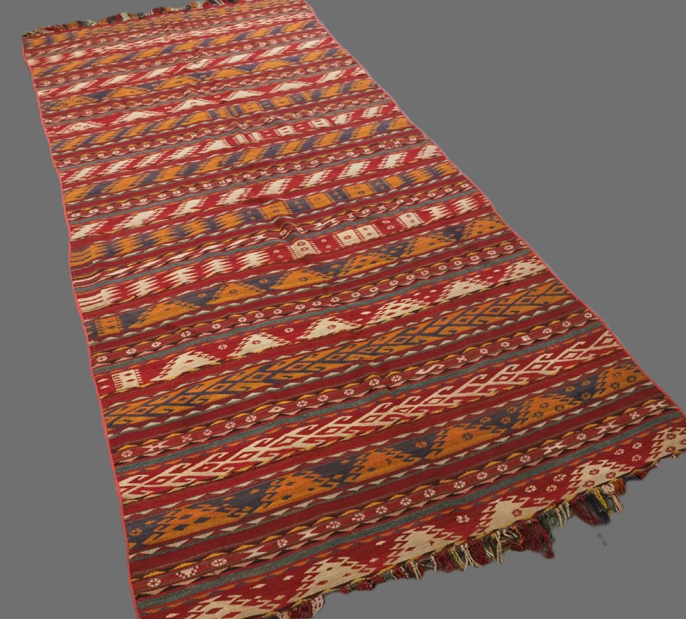 An antique Central Asian Uzbek Gajeri flatweave kilim rug featuring horizontal bands of geometric motifs woven in red, ochre, navy, and cream wool with fringed ends. View II