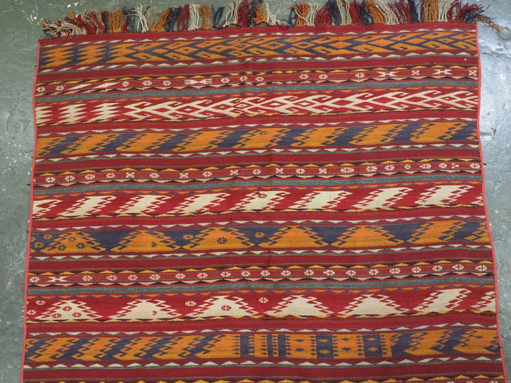 An antique Central Asian Uzbek Gajeri flatweave kilim rug featuring horizontal bands of geometric motifs woven in red, ochre, navy, and cream wool with fringed ends. View III