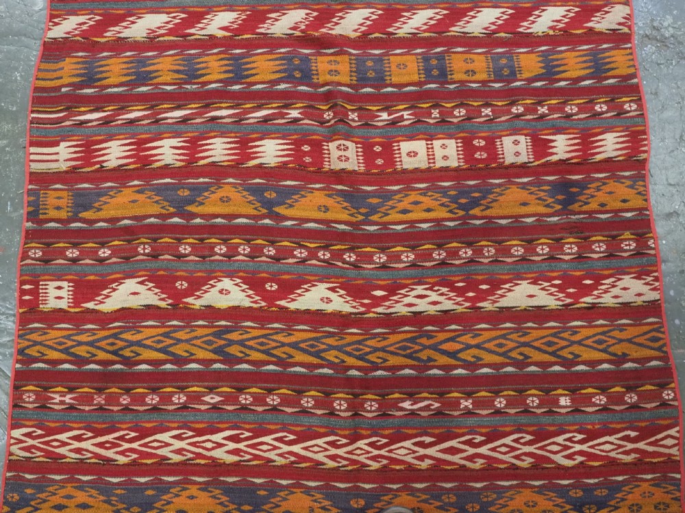 An antique Central Asian Uzbek Gajeri flatweave kilim rug featuring horizontal bands of geometric motifs woven in red, ochre, navy, and cream wool with fringed ends. View V