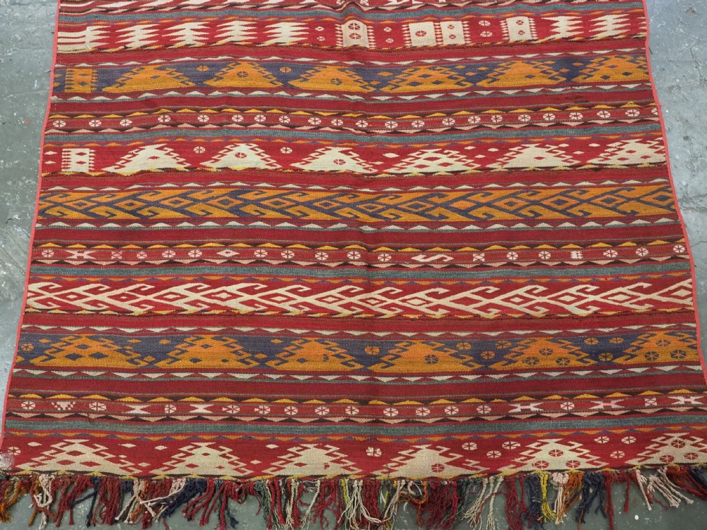 An antique Central Asian Uzbek Gajeri flatweave kilim rug featuring horizontal bands of geometric motifs woven in red, ochre, navy, and cream wool with fringed ends. View VI