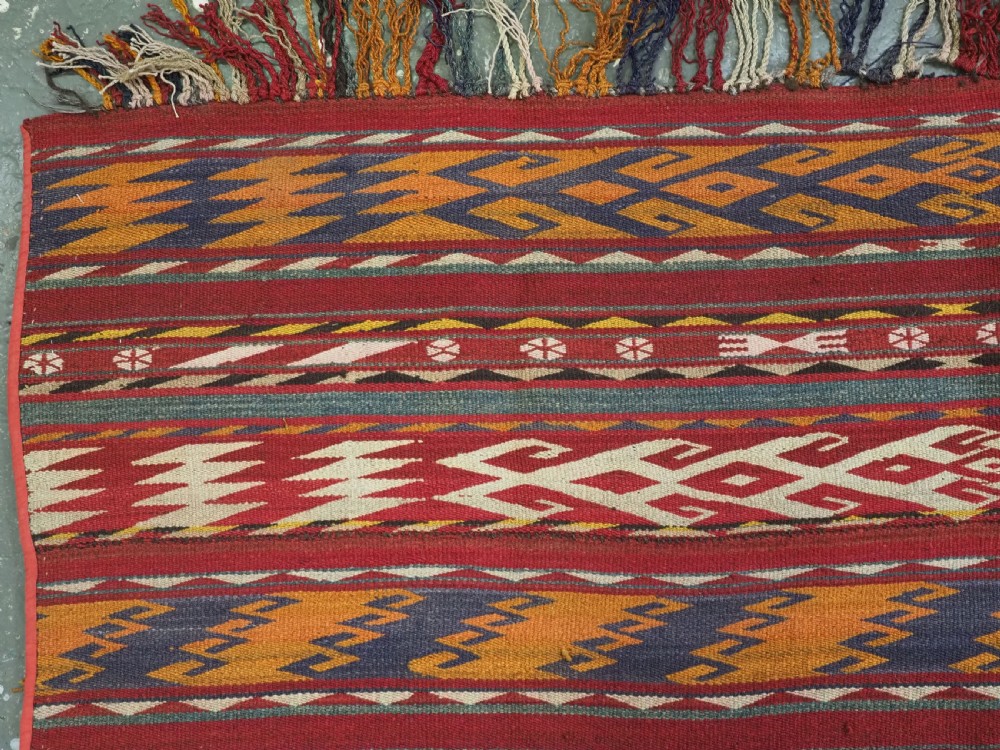An antique Central Asian Uzbek Gajeri flatweave kilim rug featuring horizontal bands of geometric motifs woven in red, ochre, navy, and cream wool with fringed ends. View VII