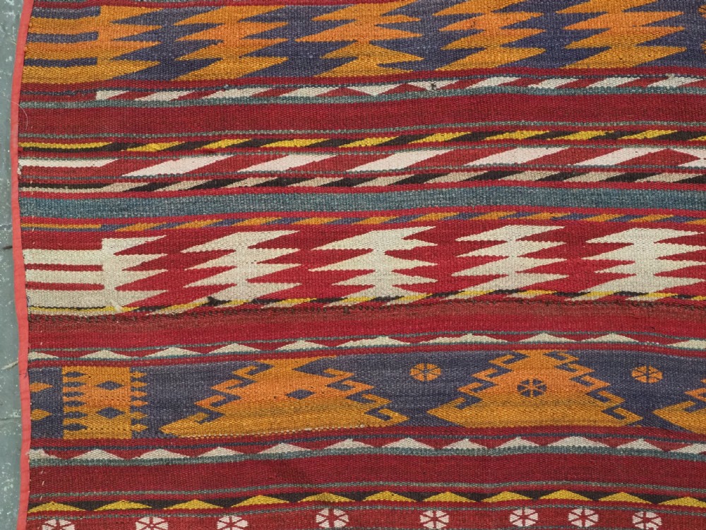 An antique Central Asian Uzbek Gajeri flatweave kilim rug featuring horizontal bands of geometric motifs woven in red, ochre, navy, and cream wool with fringed ends. View VIII