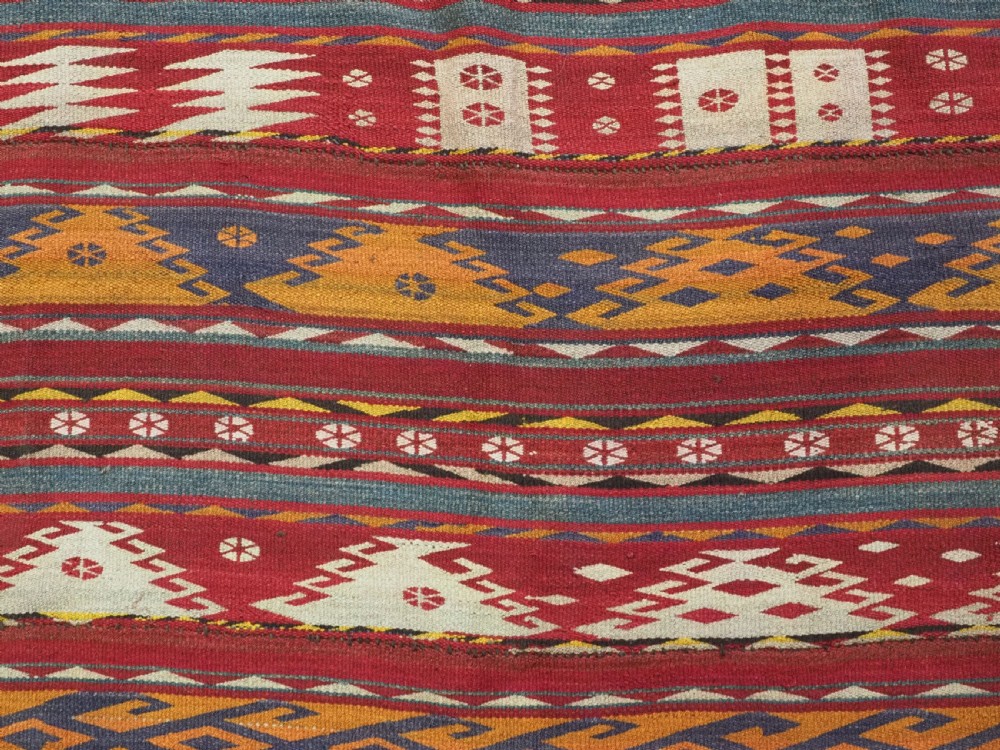 An antique Central Asian Uzbek Gajeri flatweave kilim rug featuring horizontal bands of geometric motifs woven in red, ochre, navy, and cream wool with fringed ends. View X