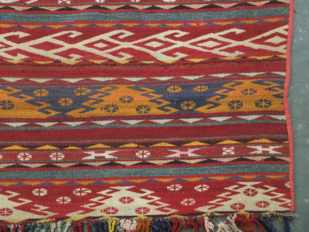 An antique Central Asian Uzbek Gajeri flatweave kilim rug featuring horizontal bands of geometric motifs woven in red, ochre, navy, and cream wool with fringed ends. View XI