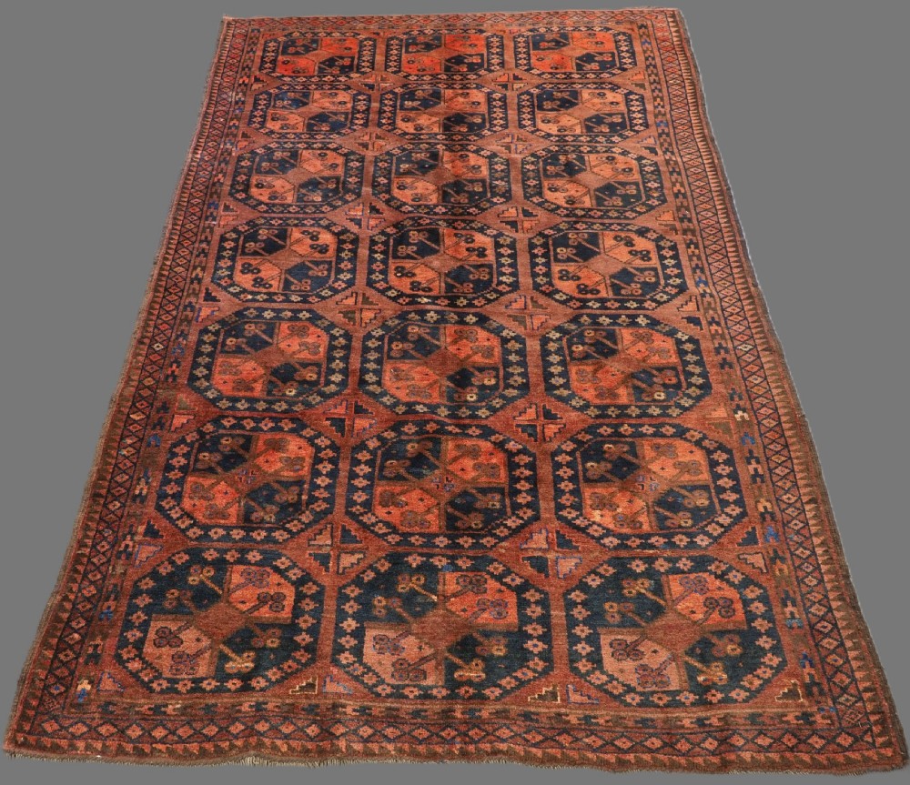 An antique hand-knotted Ersari Turkmen wool carpet featuring a repeated octagonal gul pattern in terracotta red, navy blue, and brown shades.