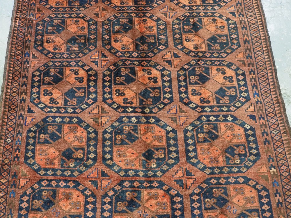 An antique hand-knotted Ersari Turkmen wool carpet featuring a repeated octagonal gul pattern in terracotta red, navy blue, and brown shades. View IV