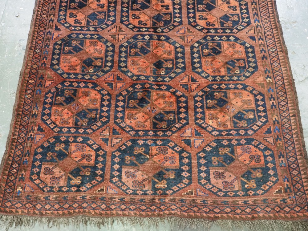 An antique hand-knotted Ersari Turkmen wool carpet featuring a repeated octagonal gul pattern in terracotta red, navy blue, and brown shades. View V