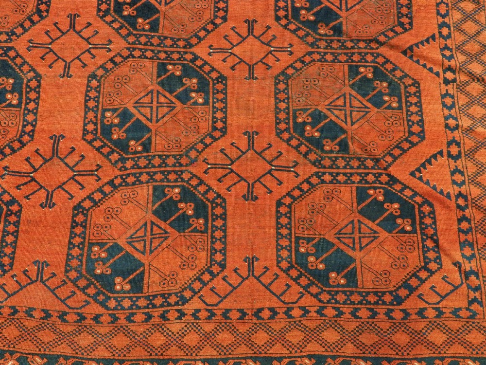 An antique handwoven Ersari Turkmen carpet featuring repeating octagonal guls in dark navy and red set upon a vibrant terracotta red background with geometric borders. View XI
