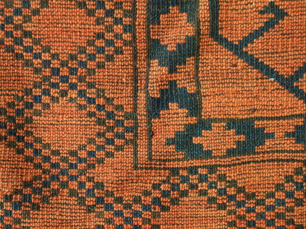An antique handwoven Ersari Turkmen carpet featuring repeating octagonal guls in dark navy and red set upon a vibrant terracotta red background with geometric borders. View XIII