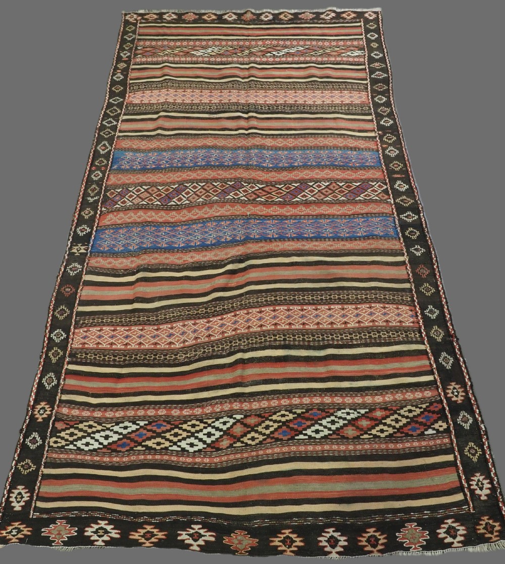 An antique handwoven Afghan Baluch kilim rug featuring horizontal geometric bands in red, blue, cream, and dark brown wool.