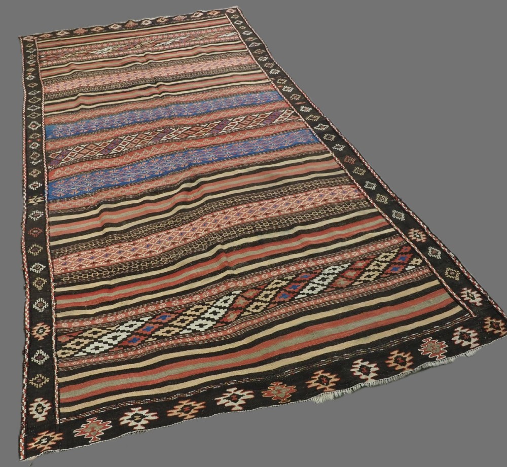 An antique handwoven Afghan Baluch kilim rug featuring horizontal geometric bands in red, blue, cream, and dark brown wool. View II
