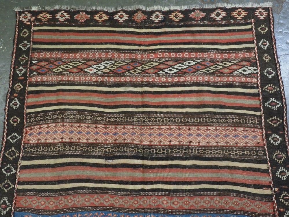 An antique handwoven Afghan Baluch kilim rug featuring horizontal geometric bands in red, blue, cream, and dark brown wool. View III