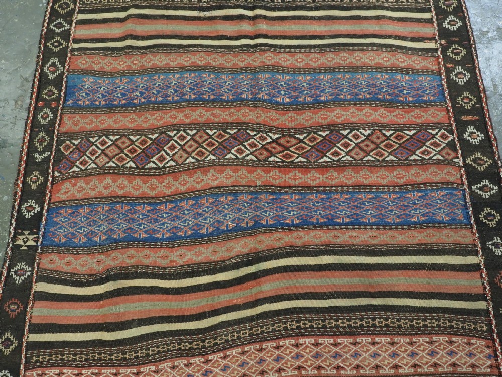 An antique handwoven Afghan Baluch kilim rug featuring horizontal geometric bands in red, blue, cream, and dark brown wool. View IV