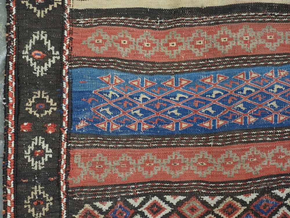 An antique handwoven Afghan Baluch kilim rug featuring horizontal geometric bands in red, blue, cream, and dark brown wool. View VII