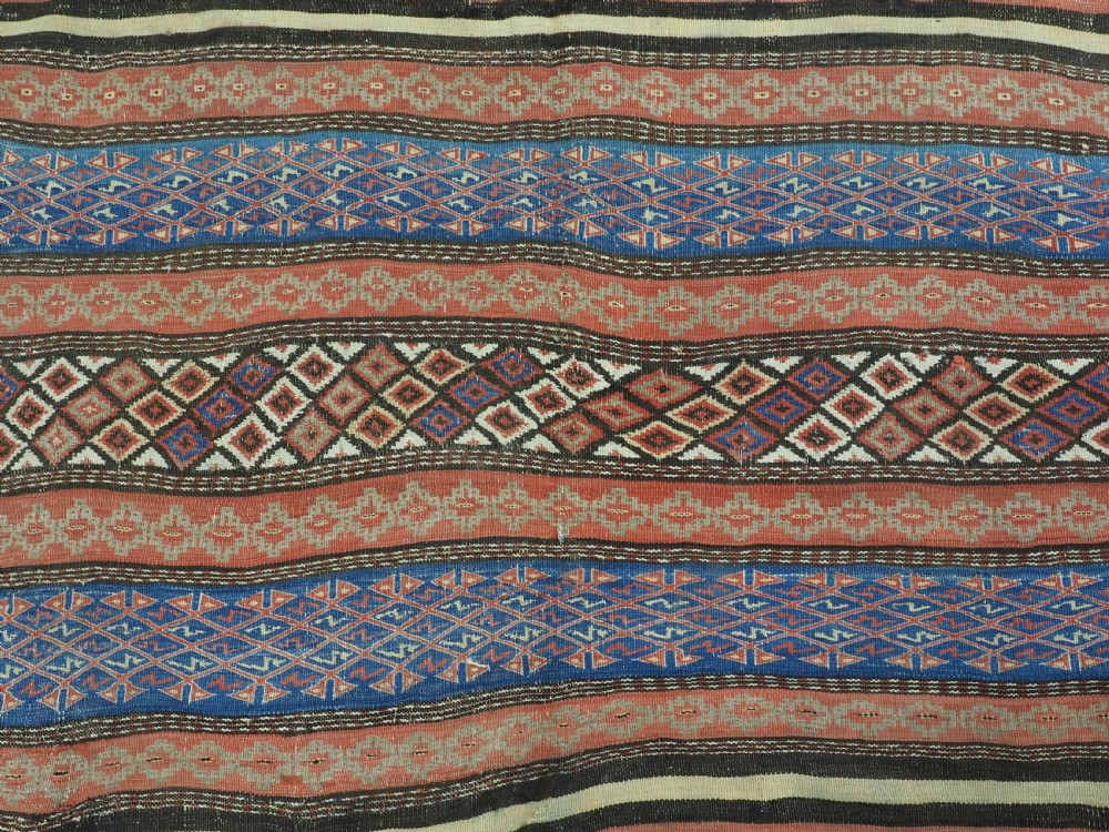 An antique handwoven Afghan Baluch kilim rug featuring horizontal geometric bands in red, blue, cream, and dark brown wool. View X