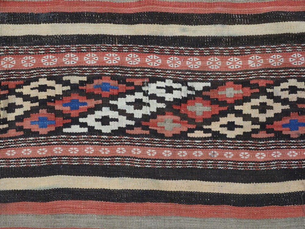 An antique handwoven Afghan Baluch kilim rug featuring horizontal geometric bands in red, blue, cream, and dark brown wool. View XII