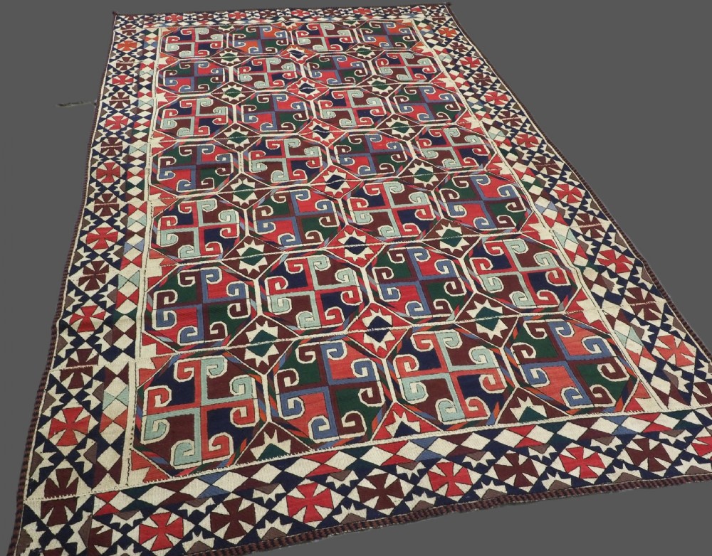 A rectangular antique Uzbek flatweave textile featuring repeating geometric octagonal medallions in red, green, blue, and cream with detailed motif borders. View II