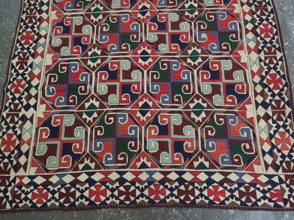 A rectangular antique Uzbek flatweave textile featuring repeating geometric octagonal medallions in red, green, blue, and cream with detailed motif borders. View III