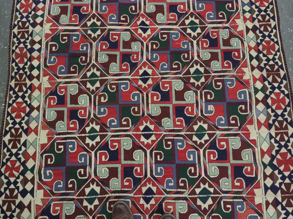 A rectangular antique Uzbek flatweave textile featuring repeating geometric octagonal medallions in red, green, blue, and cream with detailed motif borders. View V
