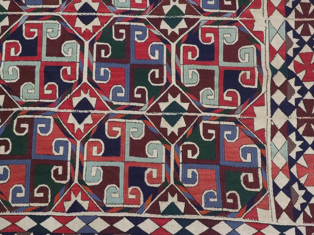 A rectangular antique Uzbek flatweave textile featuring repeating geometric octagonal medallions in red, green, blue, and cream with detailed motif borders. View X