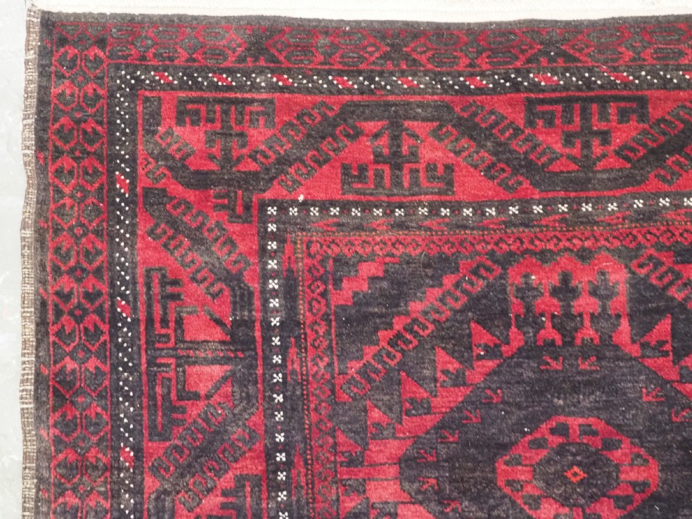 An antique Afghan Mushwani Baluch woven wool runner rug featuring deep crimson red and charcoal geometric diamond medallions along a narrow rectangular field with decorative borders. View VII