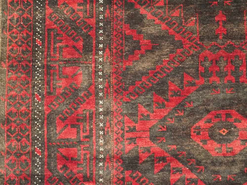 An antique Afghan Mushwani Baluch woven wool runner rug featuring deep crimson red and charcoal geometric diamond medallions along a narrow rectangular field with decorative borders. View VIII