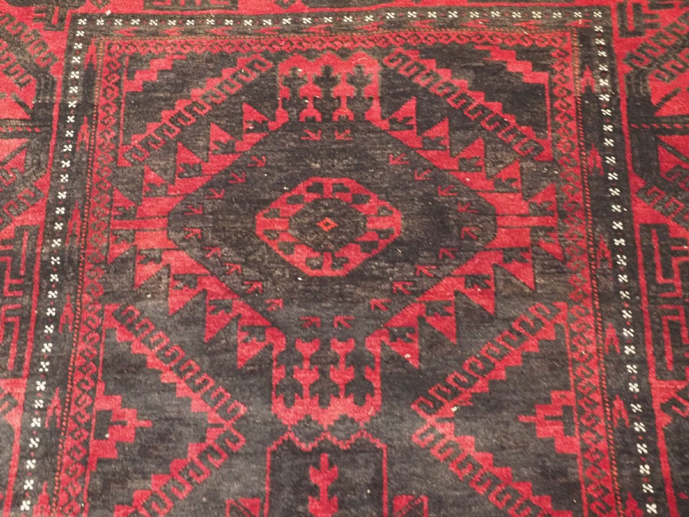 An antique Afghan Mushwani Baluch woven wool runner rug featuring deep crimson red and charcoal geometric diamond medallions along a narrow rectangular field with decorative borders. View IX