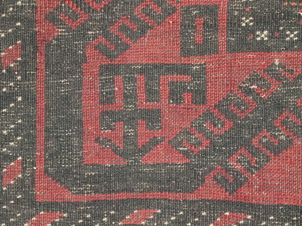 An antique Afghan Mushwani Baluch woven wool runner rug featuring deep crimson red and charcoal geometric diamond medallions along a narrow rectangular field with decorative borders. View XII