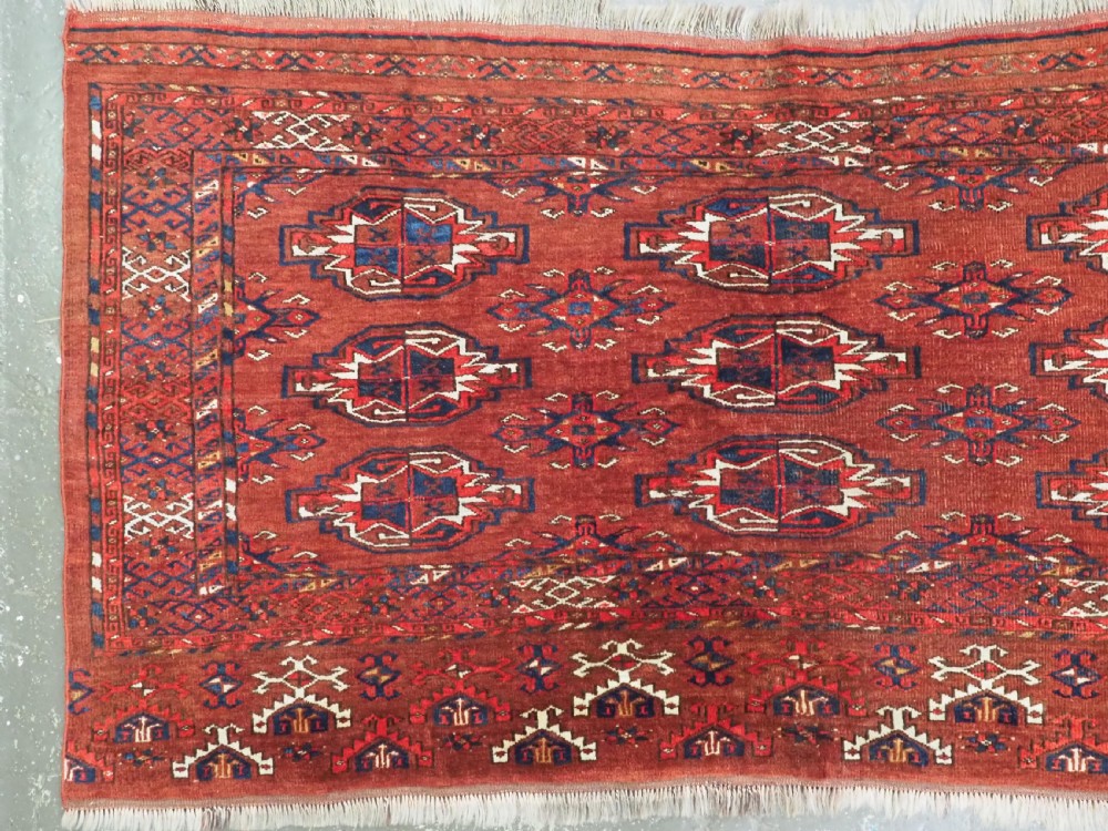 An antique rectangular Turkmen chuval wool textile featuring nine geometric gul motifs on a terracotta red ground with geometric borders. View II