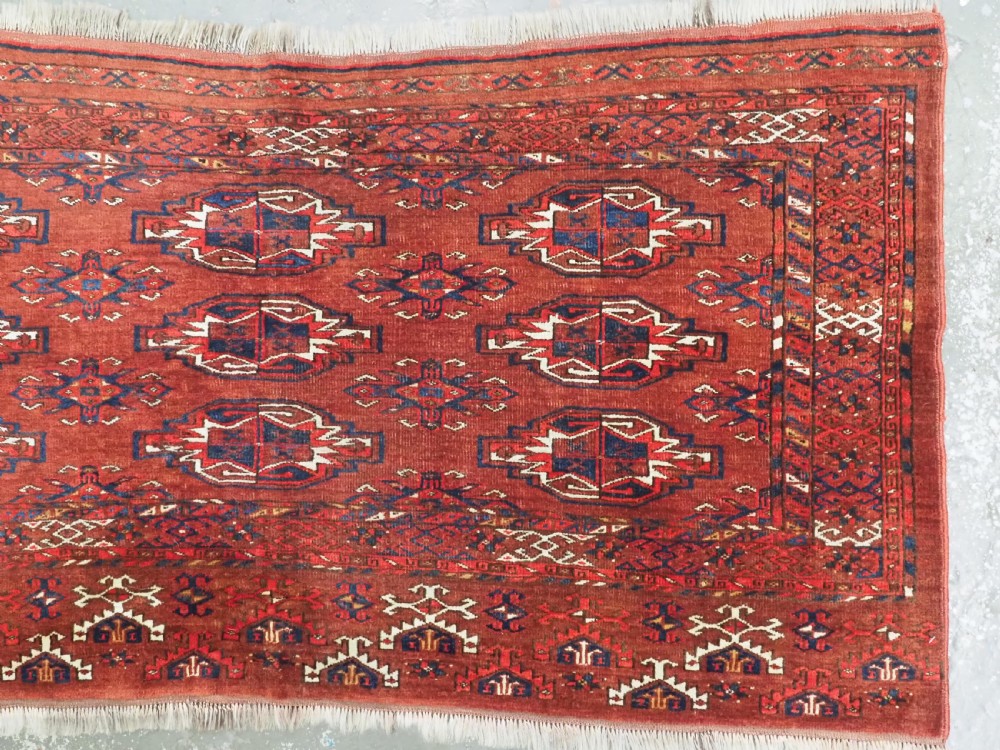 An antique rectangular Turkmen chuval wool textile featuring nine geometric gul motifs on a terracotta red ground with geometric borders. View III
