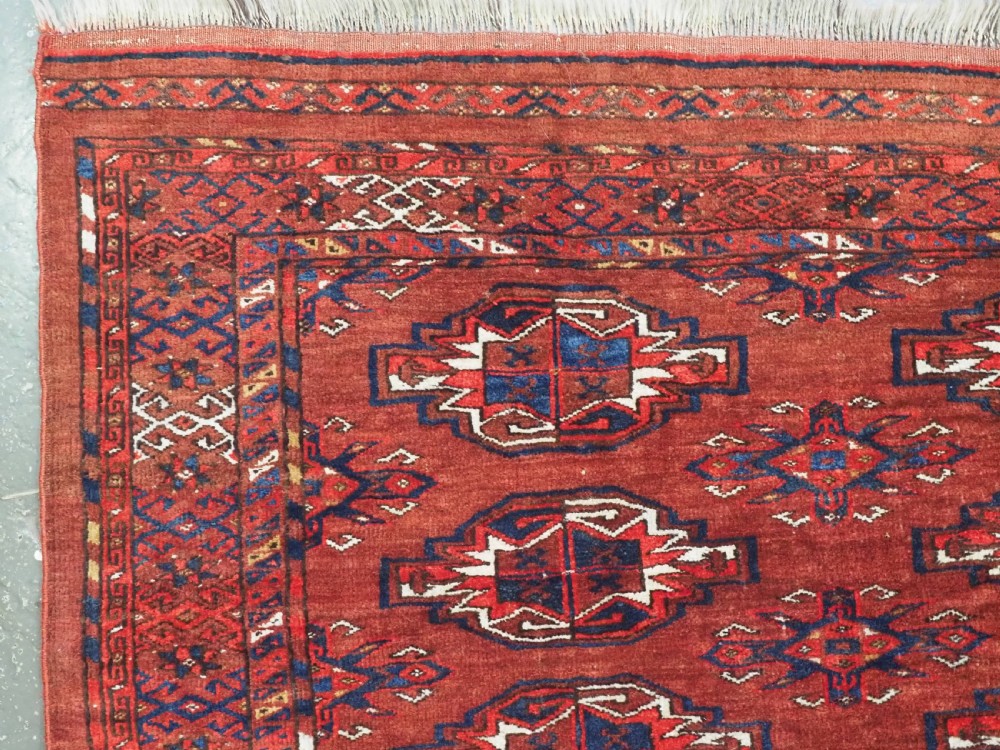 An antique rectangular Turkmen chuval wool textile featuring nine geometric gul motifs on a terracotta red ground with geometric borders. View IV