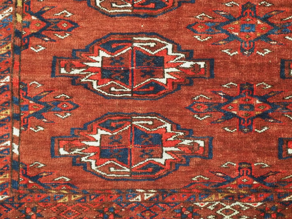 An antique rectangular Turkmen chuval wool textile featuring nine geometric gul motifs on a terracotta red ground with geometric borders. View V