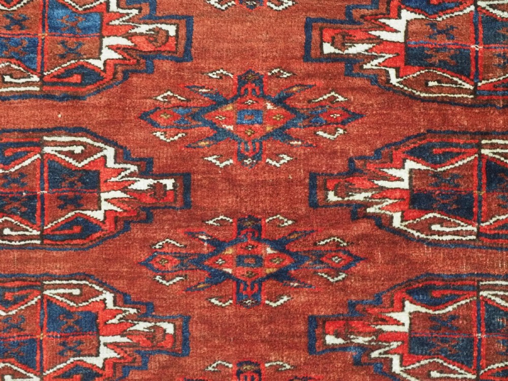 An antique rectangular Turkmen chuval wool textile featuring nine geometric gul motifs on a terracotta red ground with geometric borders. View VI