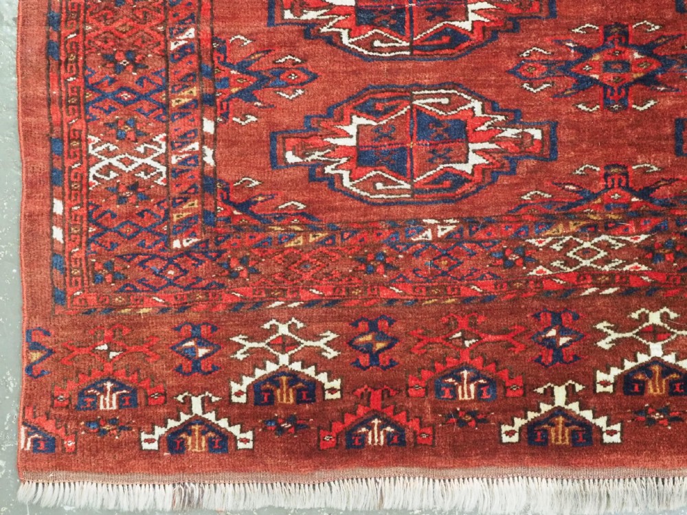 An antique rectangular Turkmen chuval wool textile featuring nine geometric gul motifs on a terracotta red ground with geometric borders. View VII
