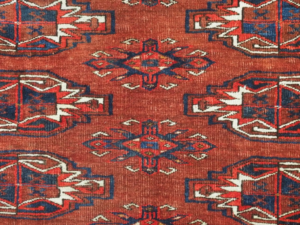 An antique rectangular Turkmen chuval wool textile featuring nine geometric gul motifs on a terracotta red ground with geometric borders. View VIII